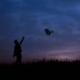 Person standing against twilight sky, letting a fan of leaves drift from their hand