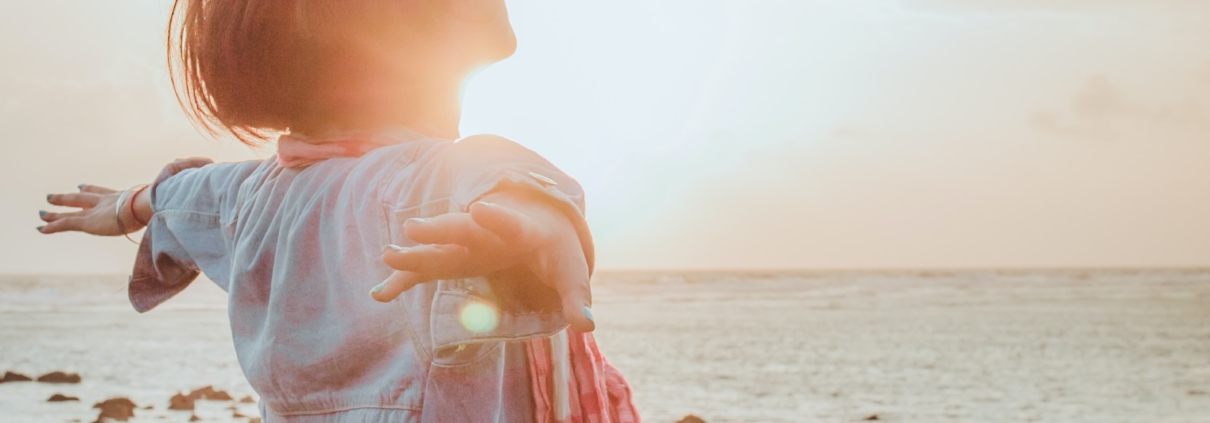 Woman at the beach. Holding her arms wide, face to the sun