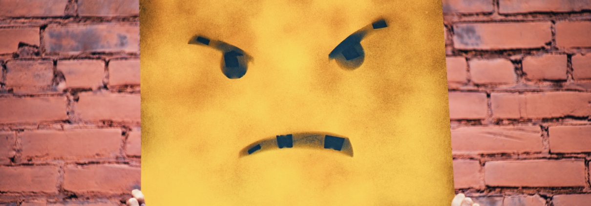 Poster of a frowning yellow cartoon face, held up by two hands.