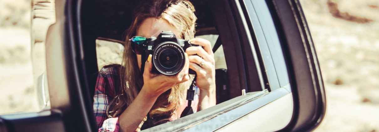 Reflection in a sideview mirror of a blonde woman taking a photo