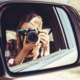 Reflection in a sideview mirror of a blonde woman taking a photo