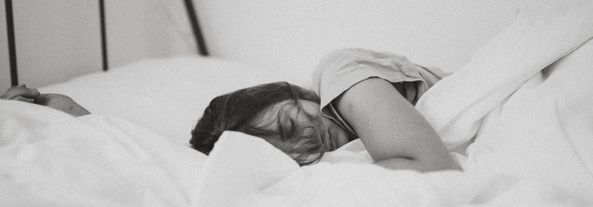 Woman curled up sleeping in a bed of white sheets and pillows
