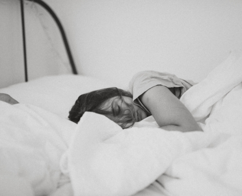 Woman curled up sleeping in a bed of white sheets and pillows