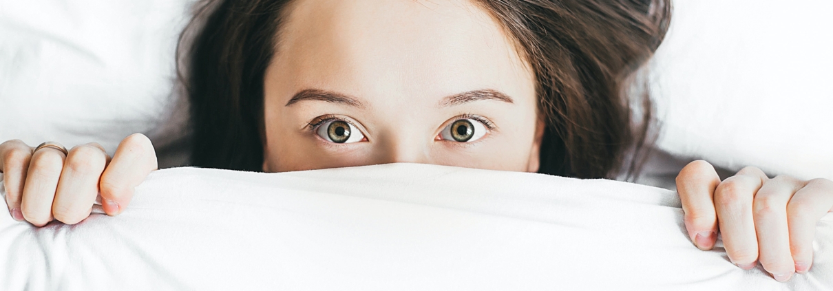 woman peeking over the top of a white sheet with eyes wide
